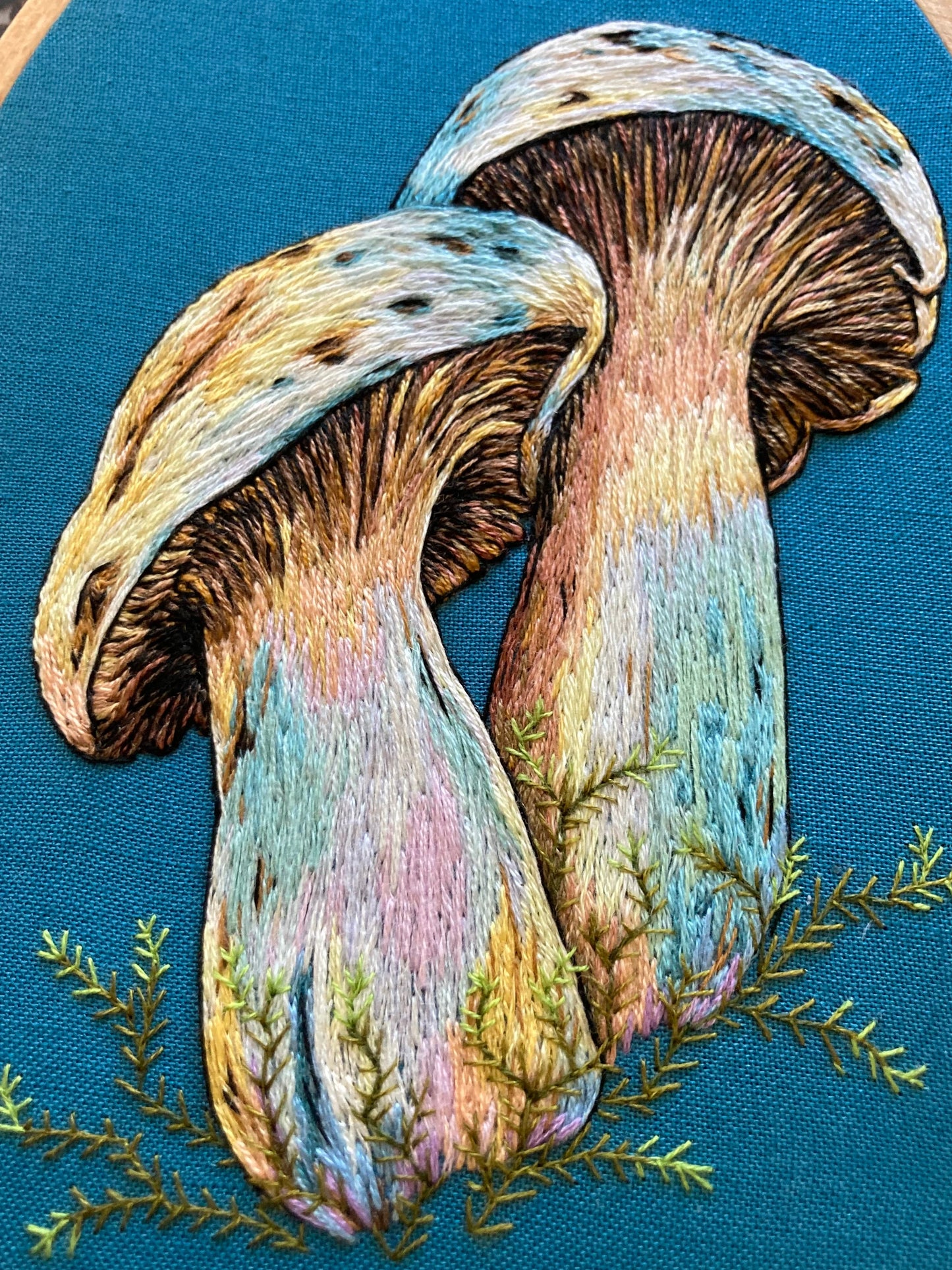 close up picture of a pair of colorful hand-embroidered mushrooms on teal fabric