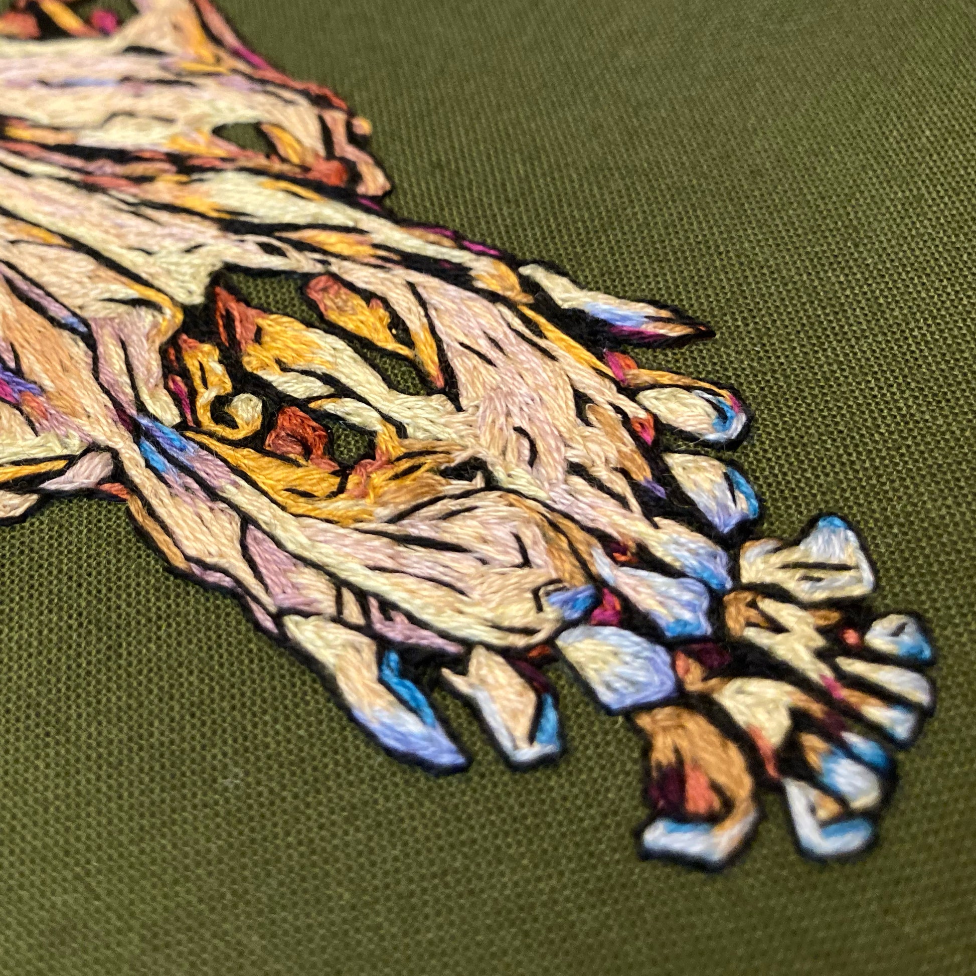 Close up of embroidery of a dog skull with prominent teeth on olive green fabric.