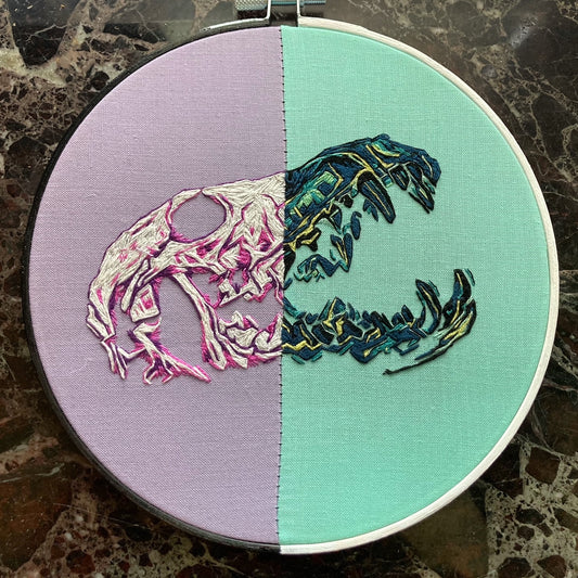 Colorful embroidery of a Coyote Skull, with the left half in link and purple tones and the right half in green and blue tones.