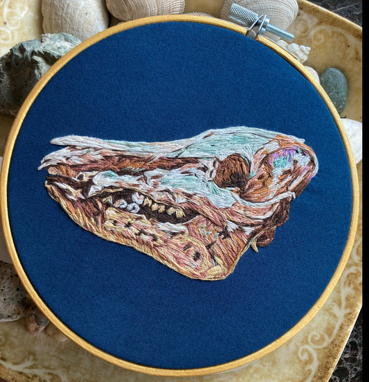 Colorful embroidery of a wild pig skull in profile on dark blue fabric in a round hoop.