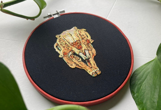 Hand embroidery of a rabbit skull on black fabric in a red, round hoop. 