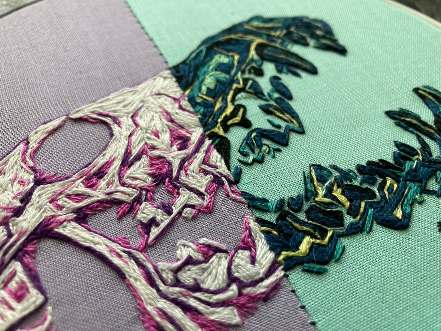 Close-up colorful embroidery of a Coyote Skull, with the left half in link and purple tones and the right half in green and blue tones.